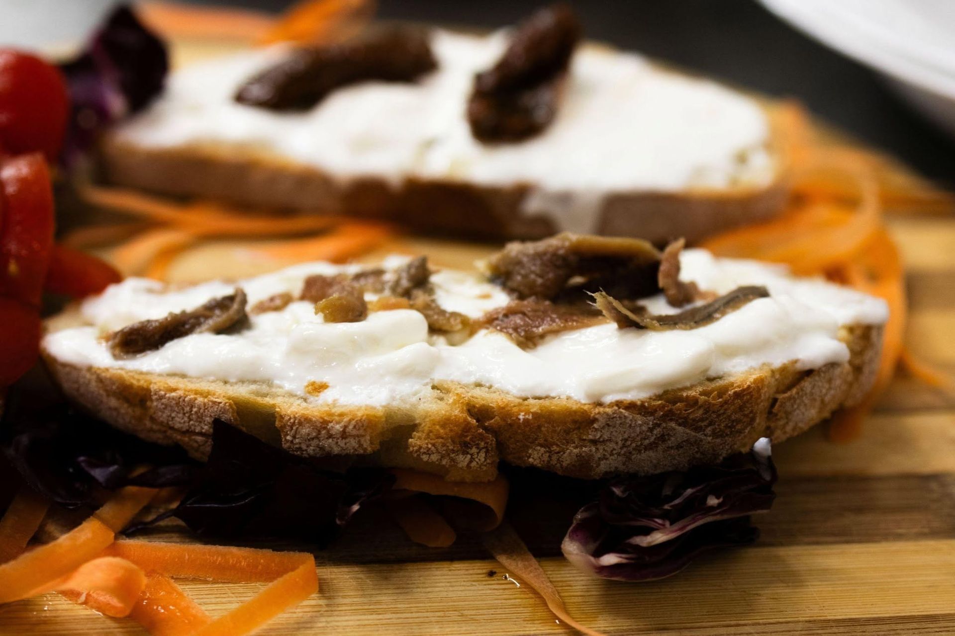 Tramezzino aperto con crema spalmabile bianca e funghi su un tagliere di legno, con fette d'arancia a lato.