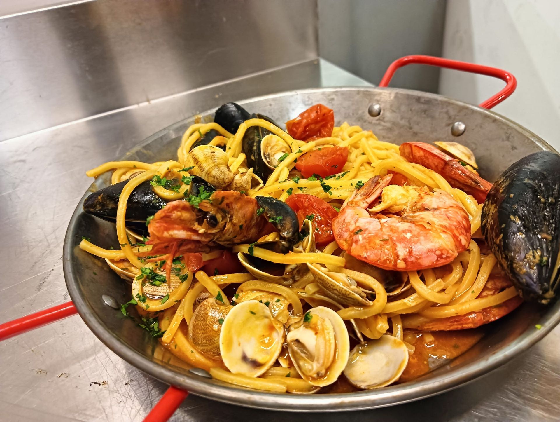 Paella di pesce in padella con manico rosso, con gamberi, cozze, vongole e tagliatelle al limone.