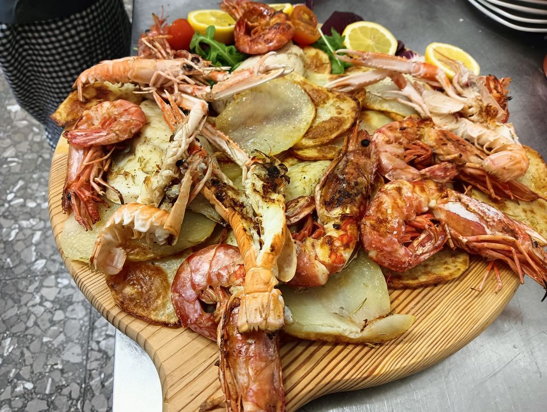 Piatto di frutti di mare con gamberi grigliati, zampe di granchio, patate e spicchi di limone su un tagliere di legno.