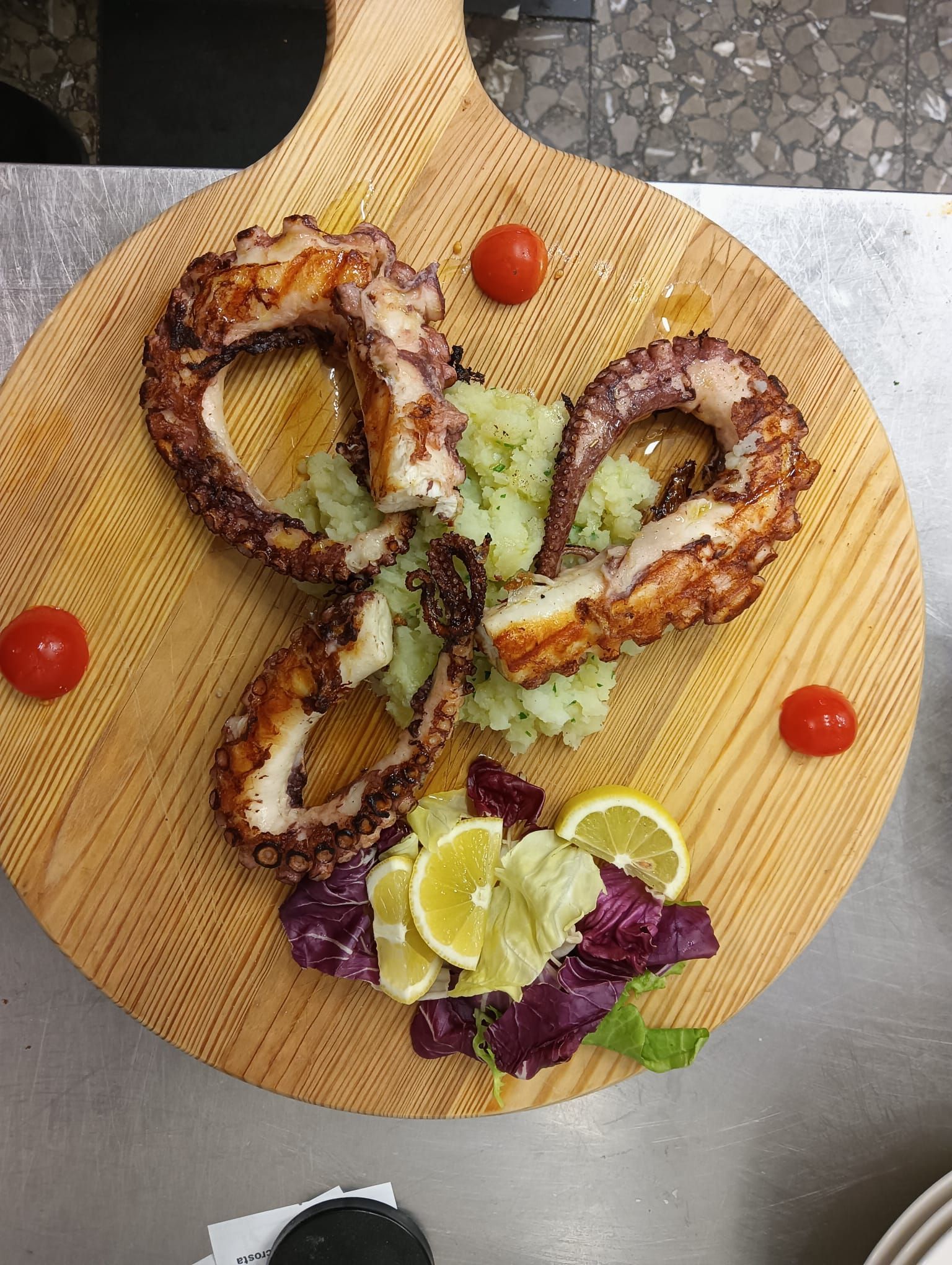 Tentacoli di polpo su un tagliere di legno con spicchi di limone e pomodorini.