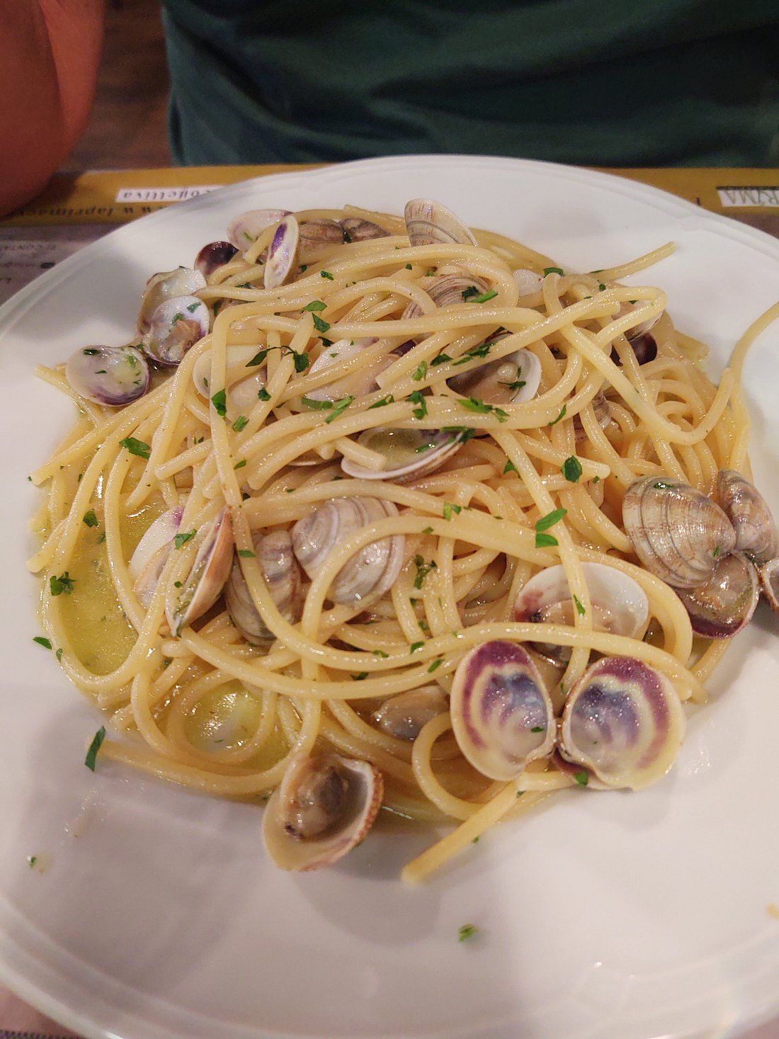 Piatto di spaghetti con vongole ed erbe aromatiche su un piatto bianco, servito su un tavolo di ristorante.