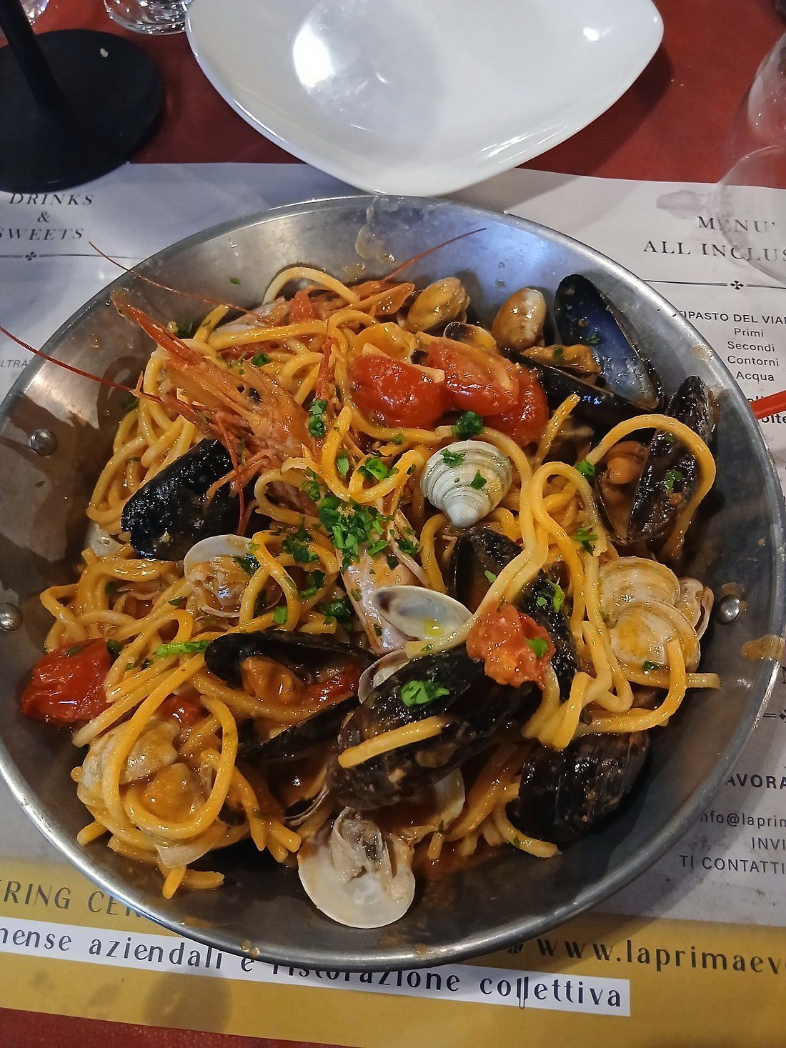 Pasta con cozze e salsa di pomodoro servita in un piatto, guarnita con formaggio grattugiato ed erbe aromatiche.