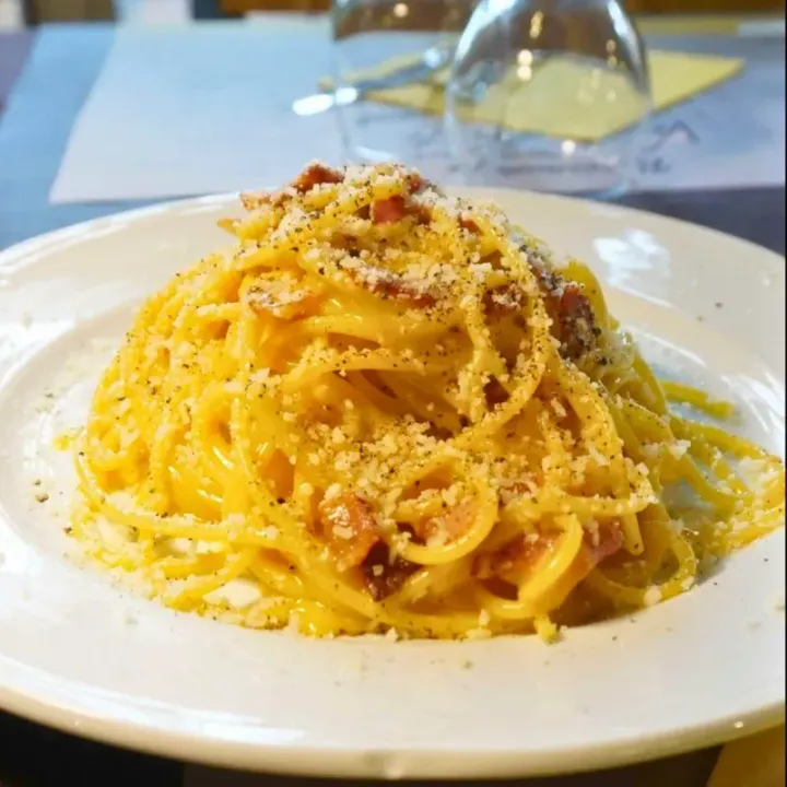 Piatto di spaghetti alla carbonara con formaggio grattugiato su una tovaglia bianca.