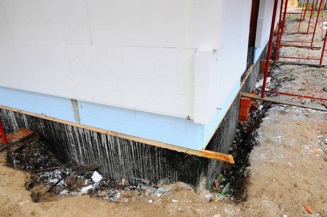 House corner with black waterproofing membrane and exposed foundation during construction