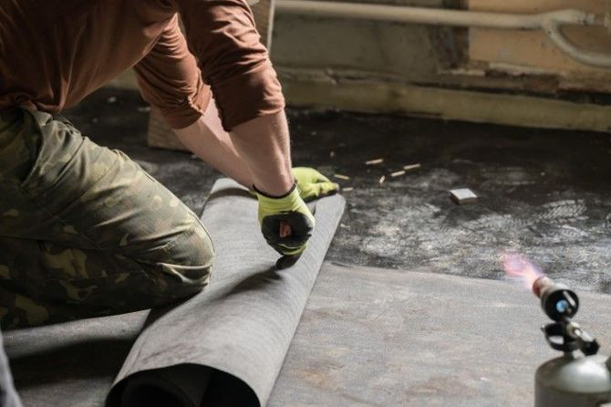 Person using a utility knife to cut rolled flooring material on a bare floor.