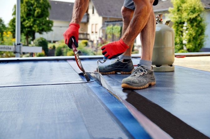 Worker applying sealant to a flat roof with a brush and roller under bright daylight