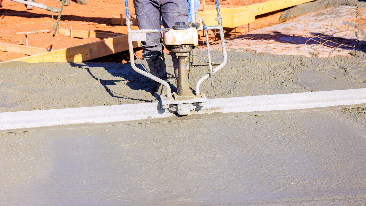 Person using a plate compactor to compact wet concrete on a construction site.