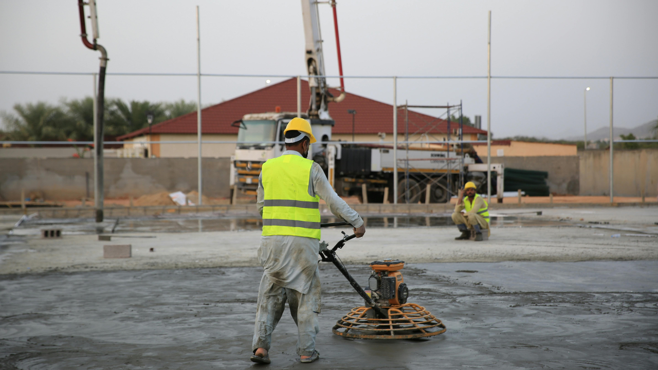 Construction workers leveling concrete with a power trowel; setting is outdoors.