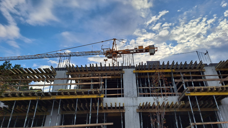 Construction site with crane against a cloudy blue sky. A building frame is visible.