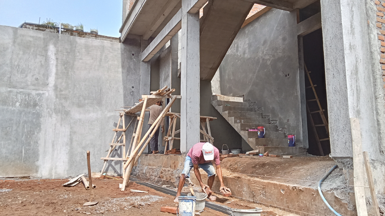 Construction site with a worker laying bricks near stairs. Wooden scaffolding supports a staircase under construction.