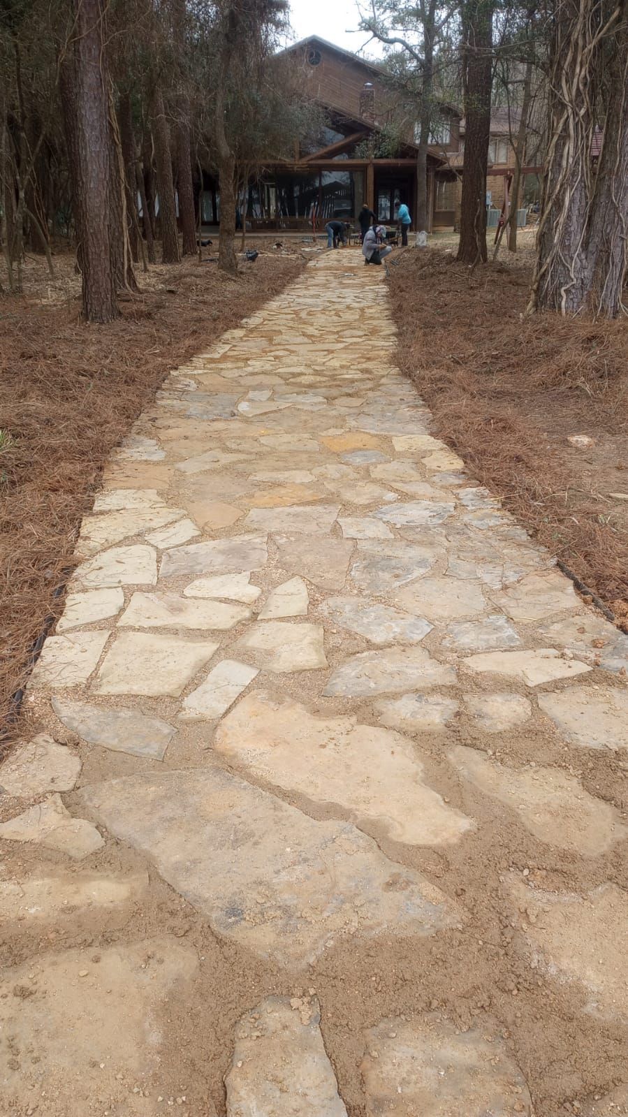 Stone path through a wooded area leading to a pavilion with a few people in the distance