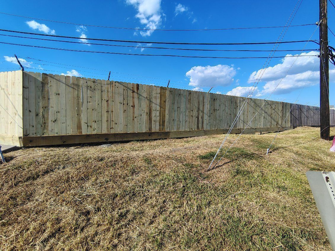 Long tan wooden fence on a grassy slope under a bright blue sky with power lines above
