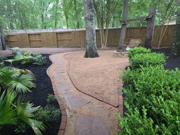 Backyard garden path with gravel, stepping stones, trees, and a wooden fence