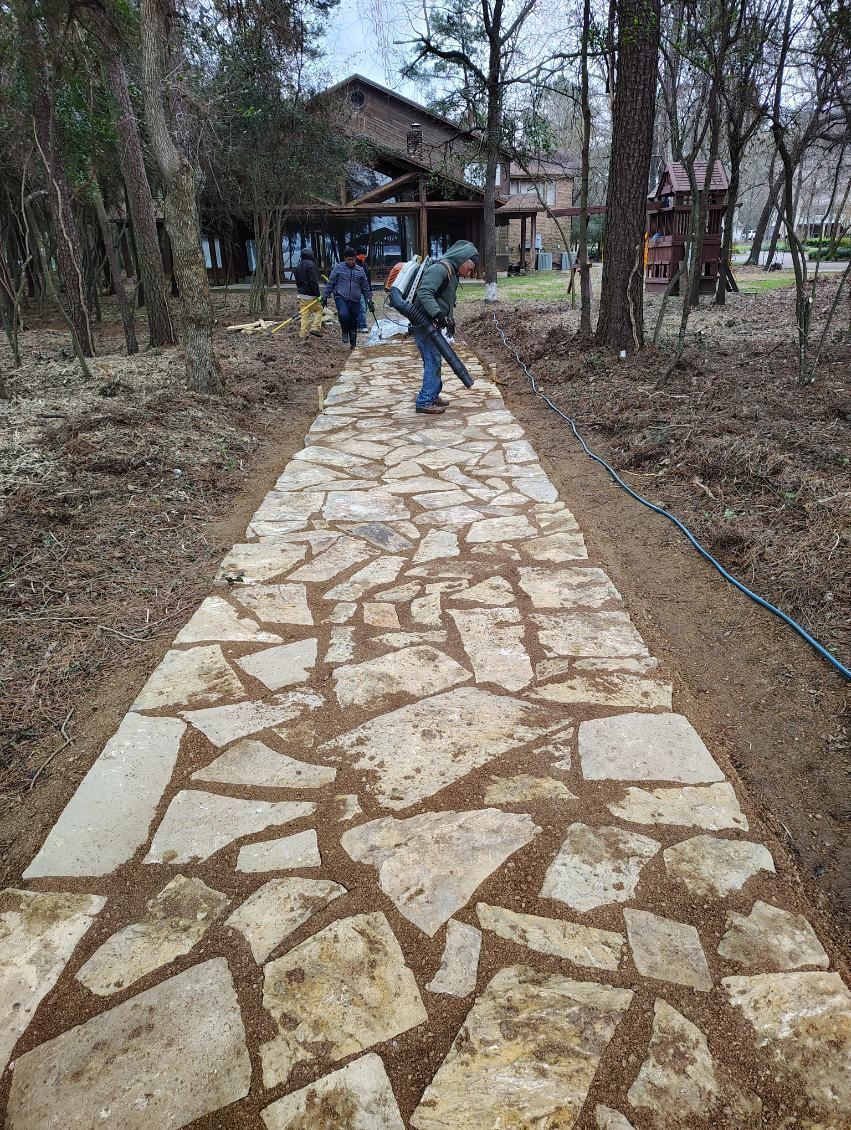 Stone walkway in a wooded park with two people walking toward a small building.