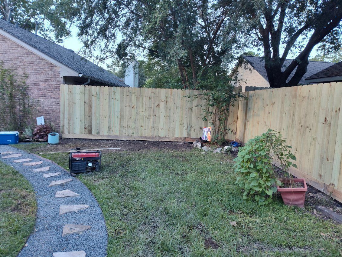 Backyard with wooden fence, stone path, lawn, and trees; small red cart and potted plant visible.