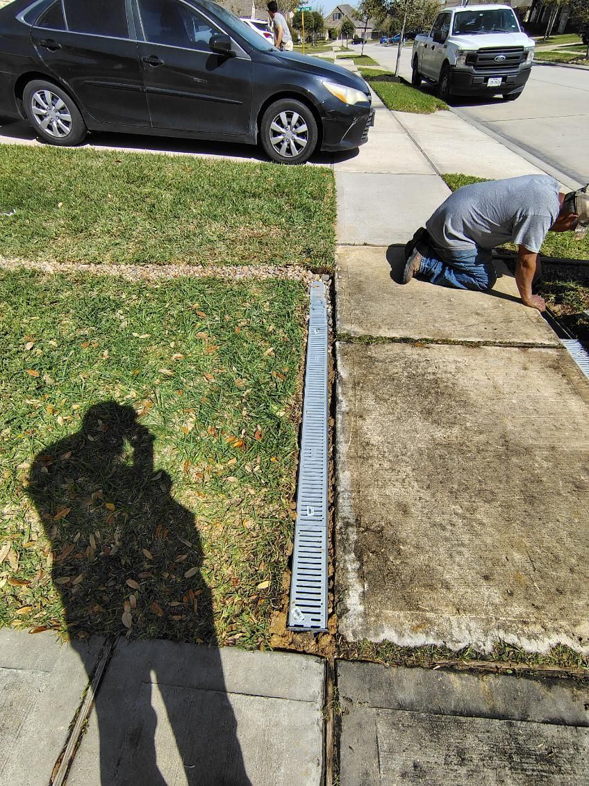 Measuring tape stretched along a sidewalk edge beside a worker crouching near a curb and parked car
