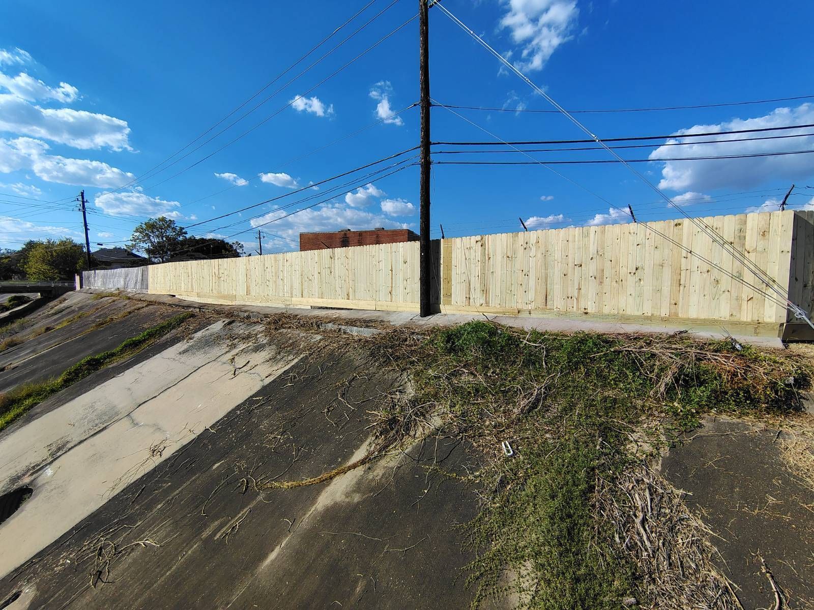 Concrete drainage ditch beside a beige retaining wall under a blue sky with power lines