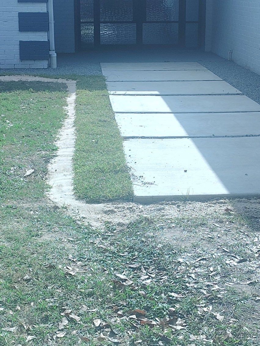 Concrete walkway beside a grassy yard leading to a house entrance in bright sunlight
