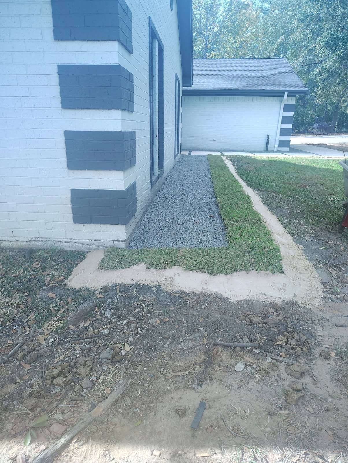 Side of a house with a gravel path and narrow grass strip leading to a garage.