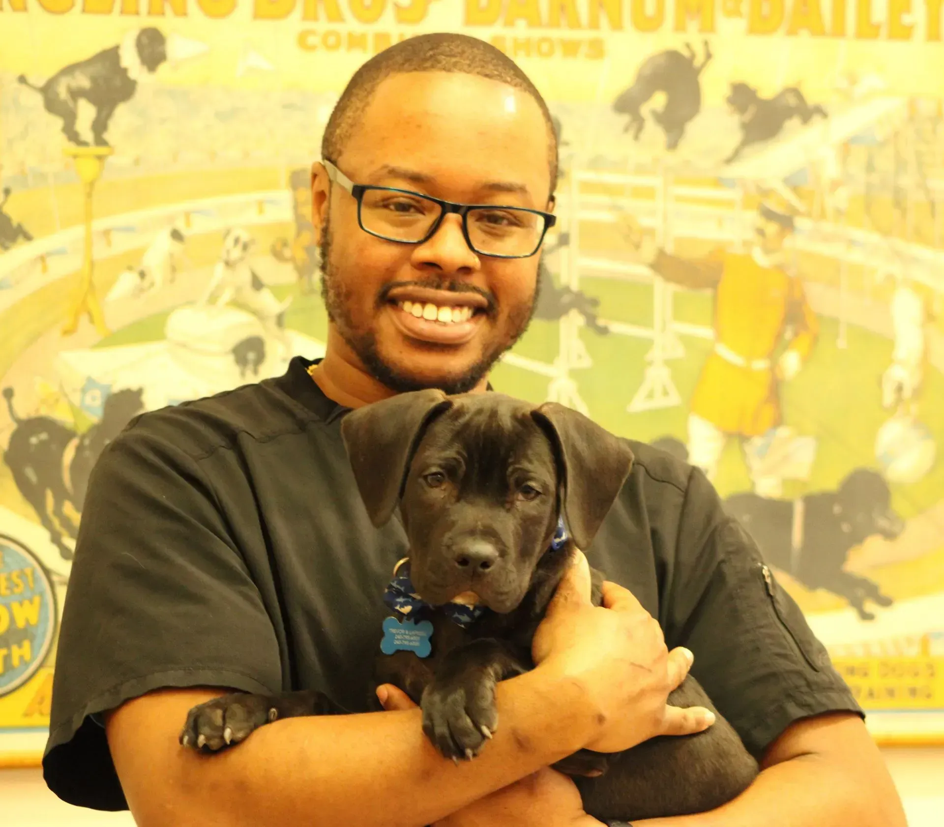 A man is holding a puppy in front of a poster that says ' danum ' on it