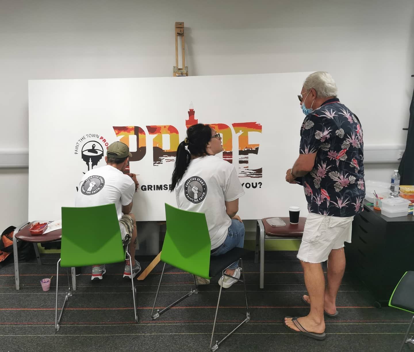A group of people are sitting in front of a large sign that says pride
