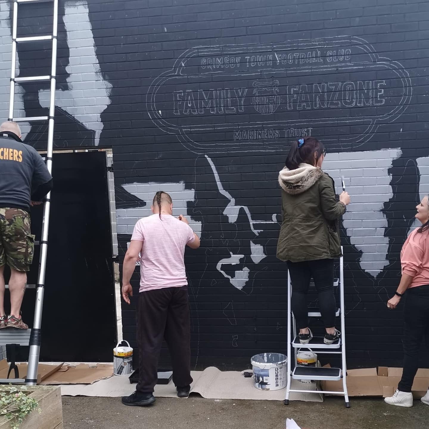 A group of people are painting a mural on a brick wall.