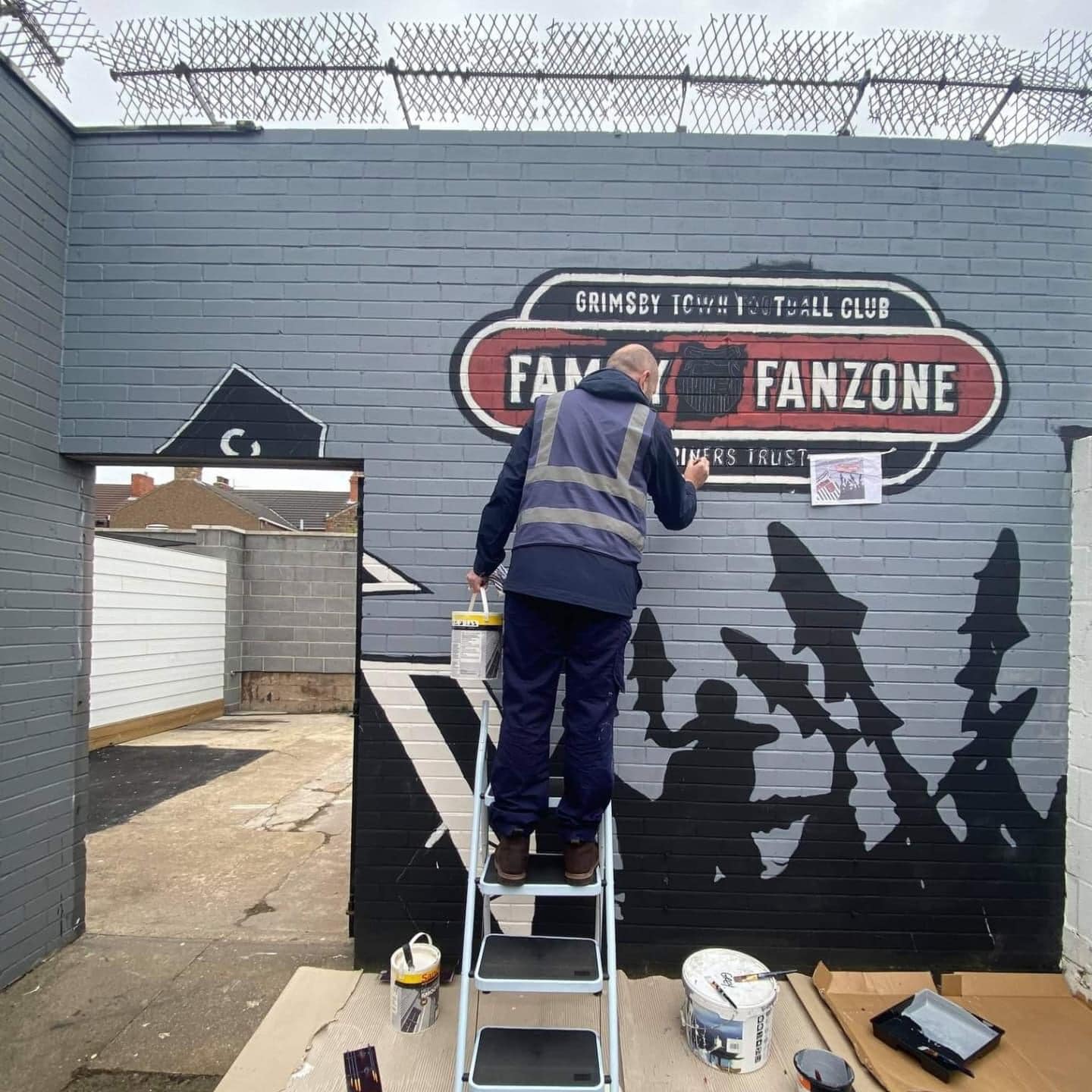 A man on a ladder paints a sign that says fanzone
