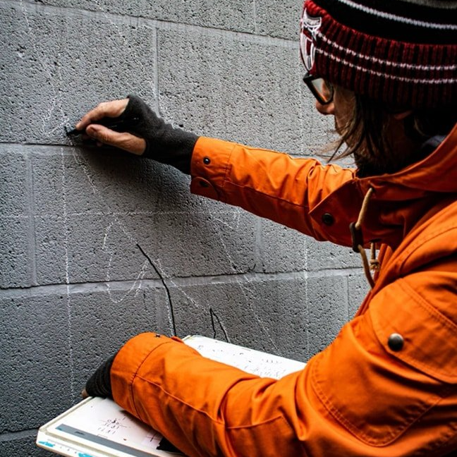 A person in an orange jacket is writing on a brick wall