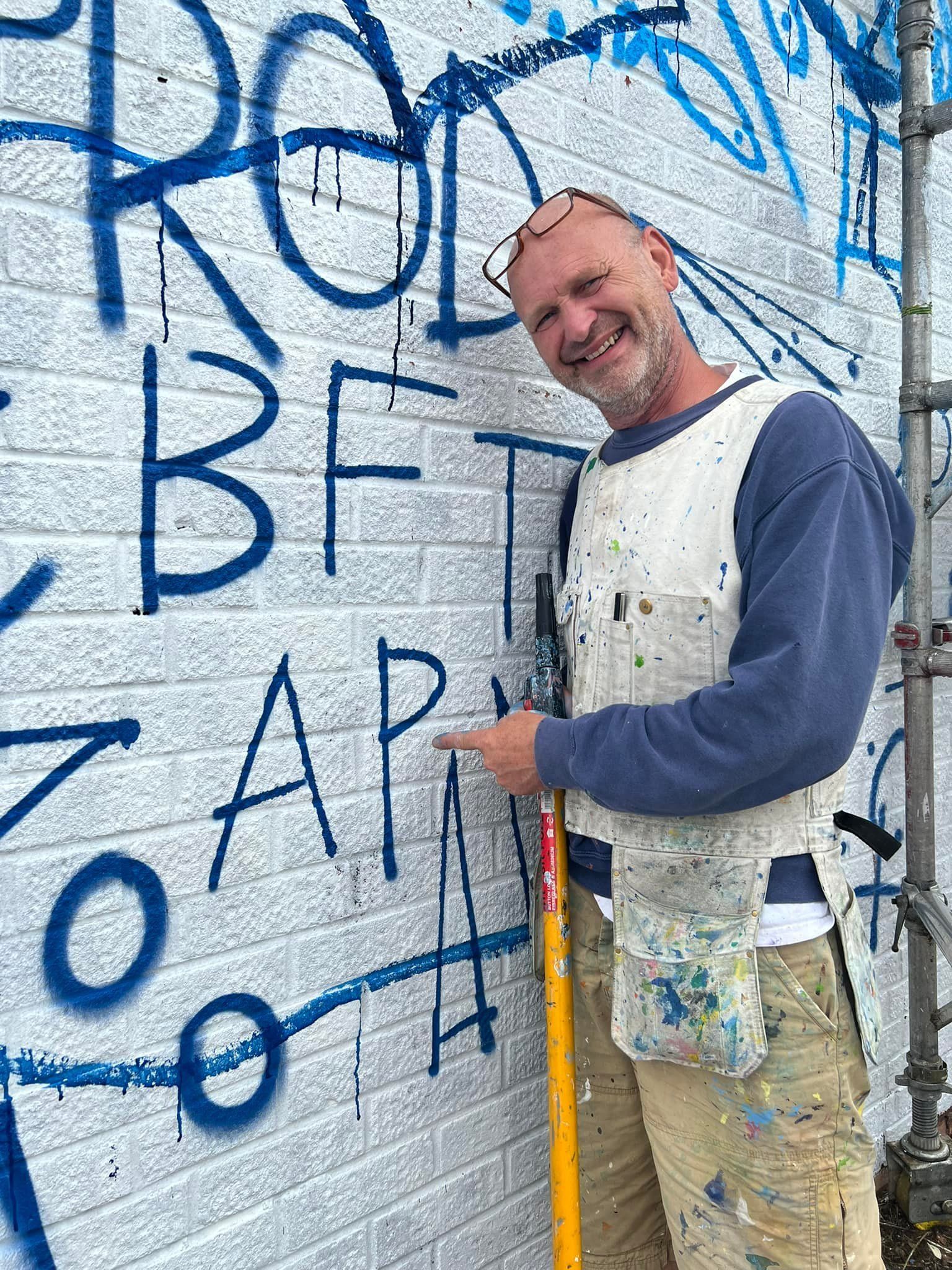 A man is standing in front of a brick wall with graffiti on it.