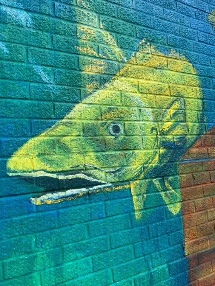 A painting of a fish on a brick wall.