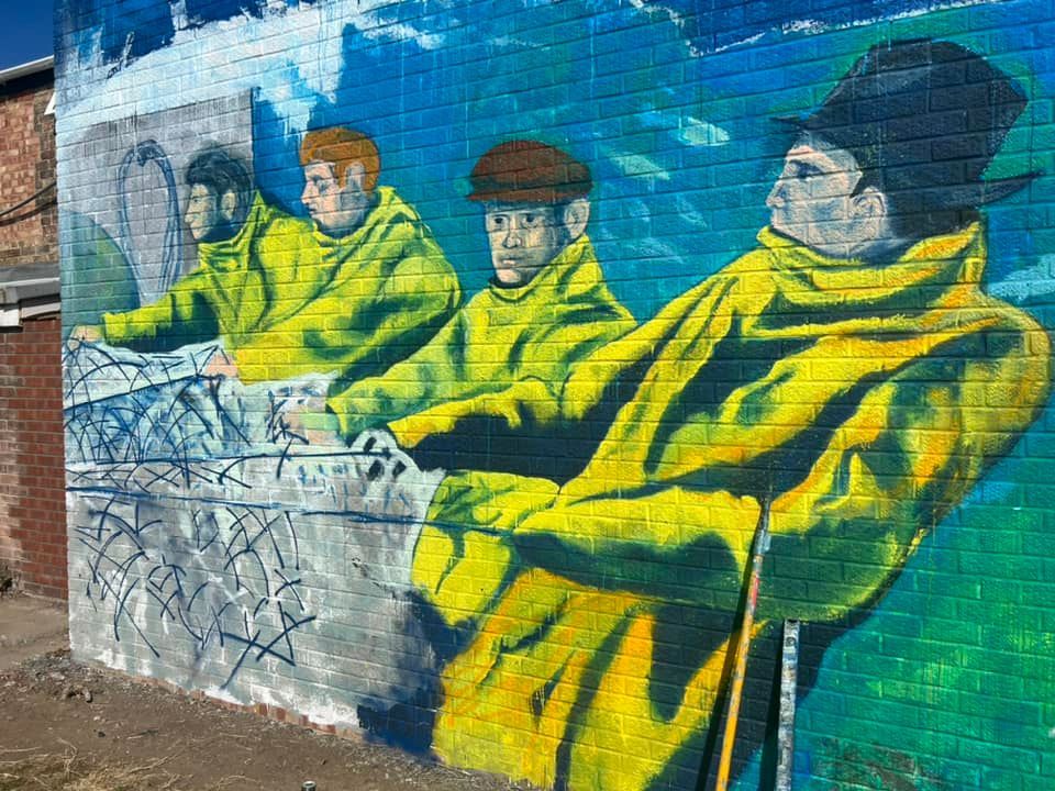 A mural of four men in yellow jackets on a brick wall