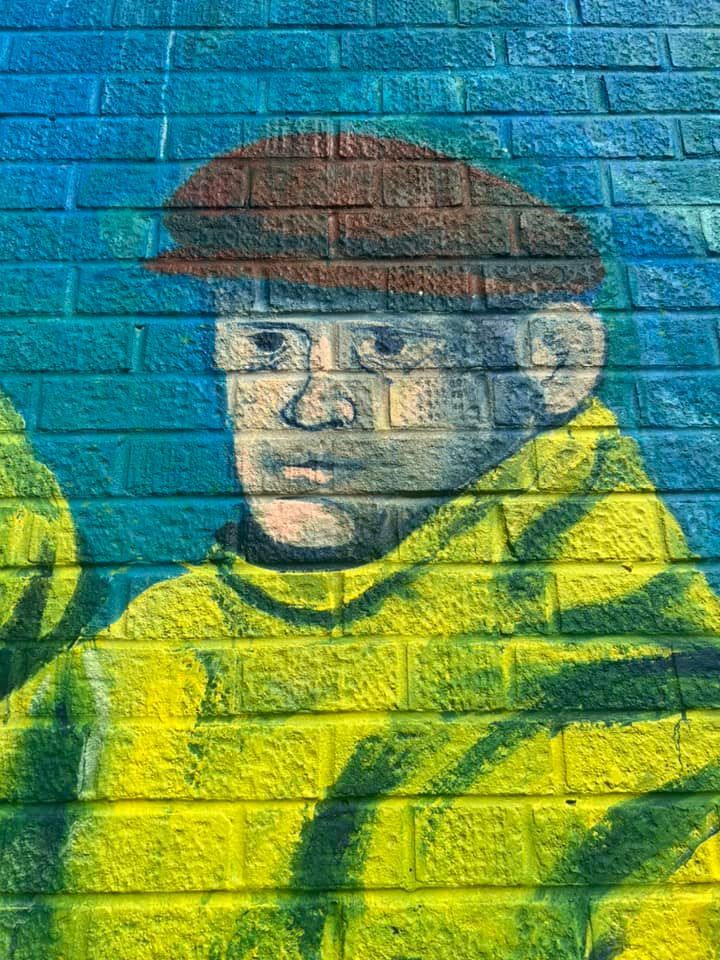 A painting of a man wearing a hat and glasses on a brick wall.