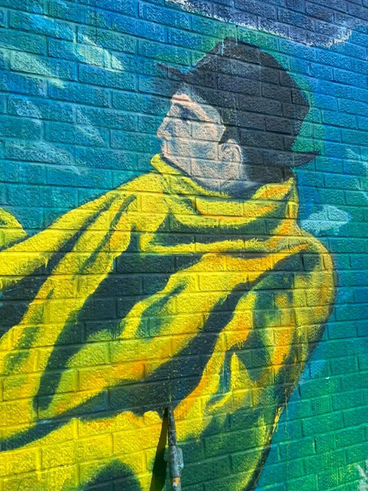 A painting of a man in a yellow coat and hat on a brick wall.