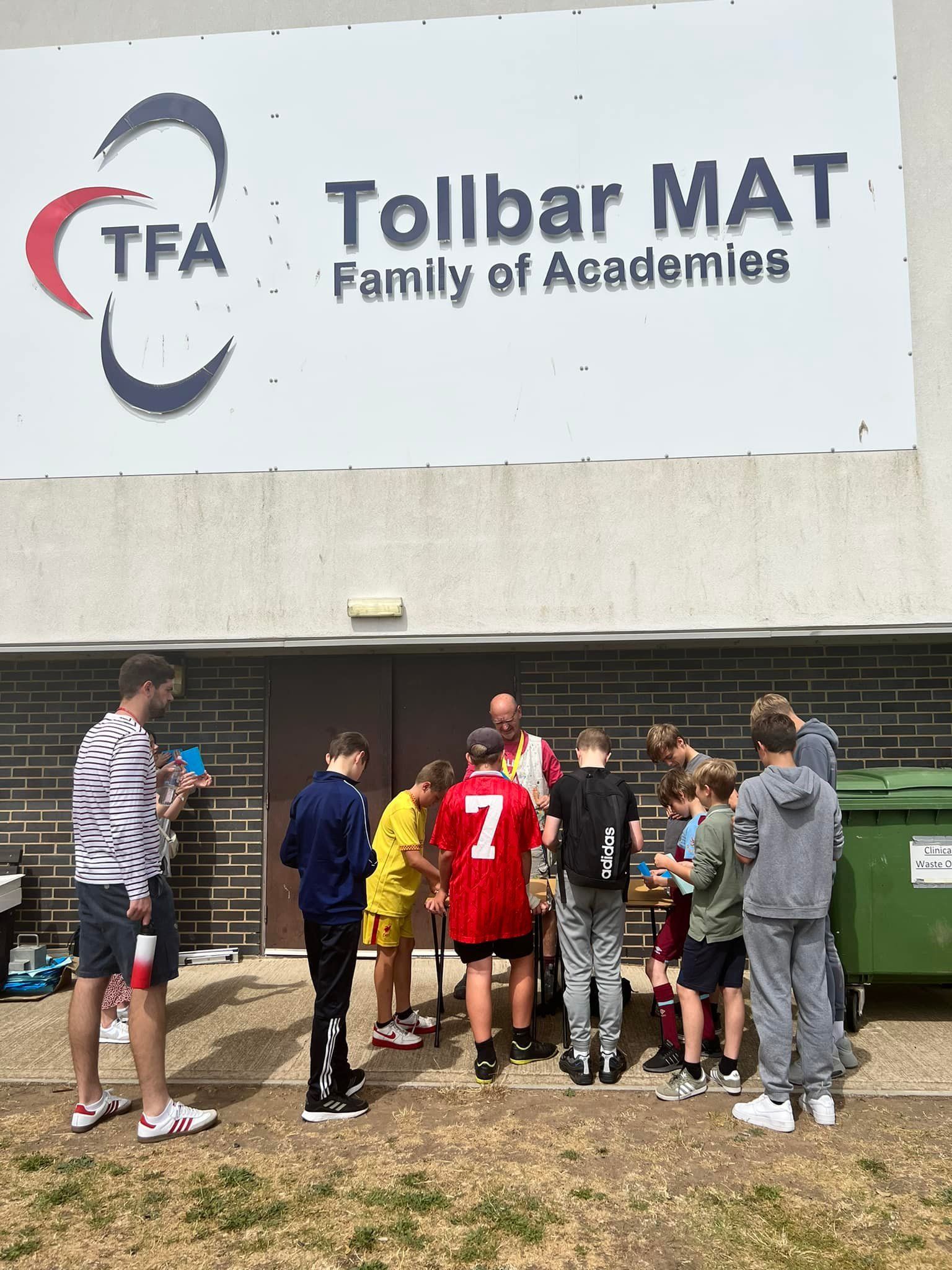 A group of people are standing in front of a building with a sign that says tollbar mat family of academics.