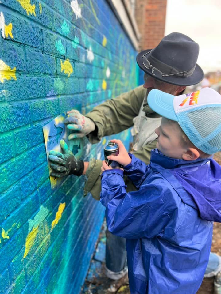 A man and a boy are painting a mural on a brick wall.