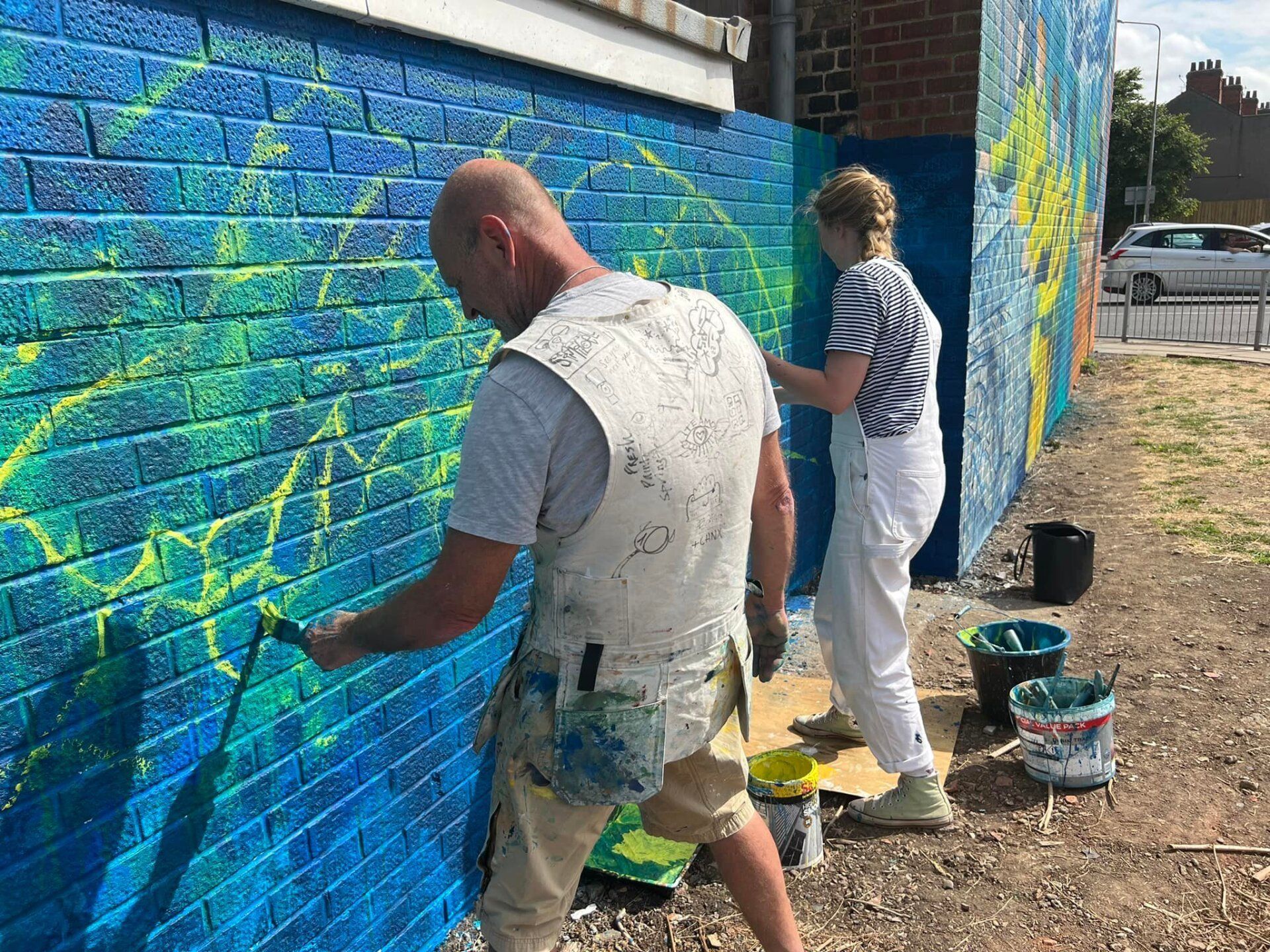 A man and a woman are painting a mural on a brick wall.