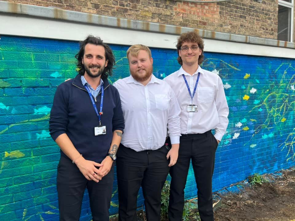 Three men are posing for a picture in front of a blue wall.