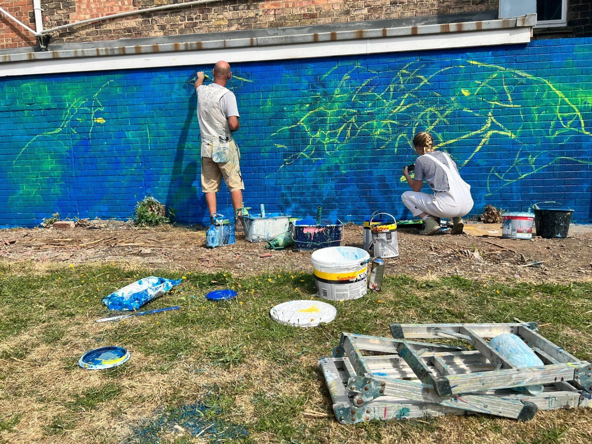 A man and a woman are painting a mural on a brick wall.