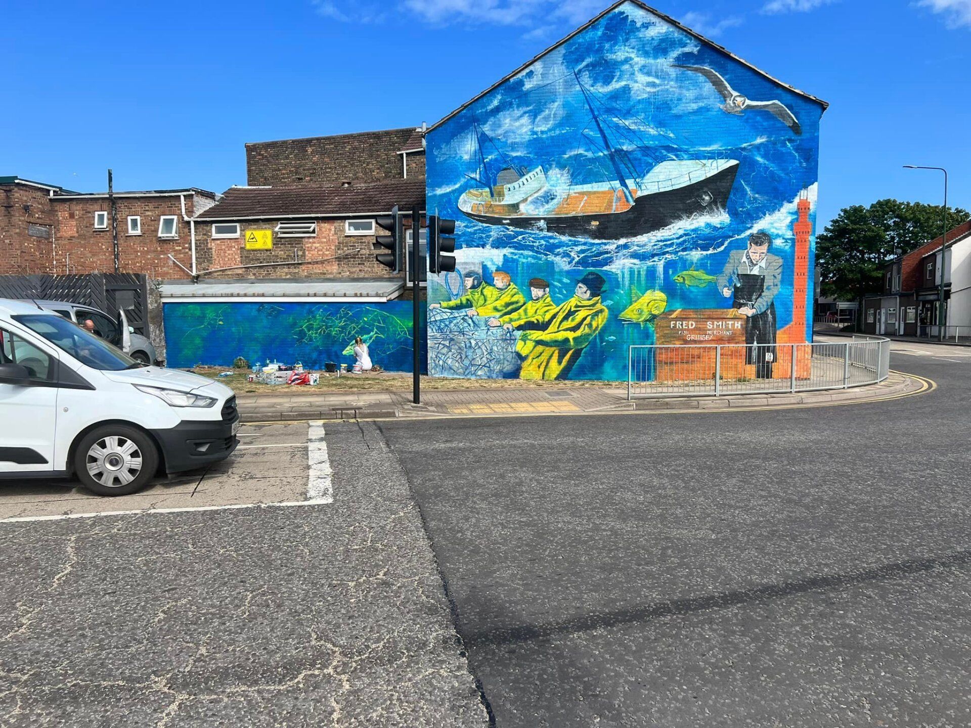 A white van is parked in front of a large mural on the side of a building.