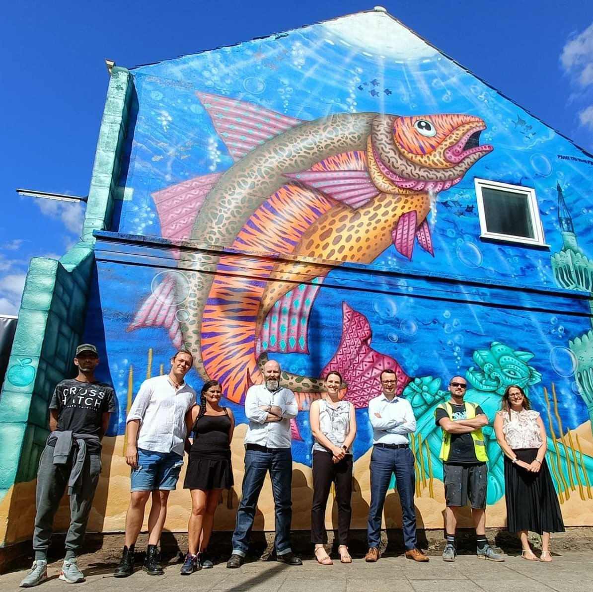 A group of people standing in front of a mural of a fish on the side of a building.
