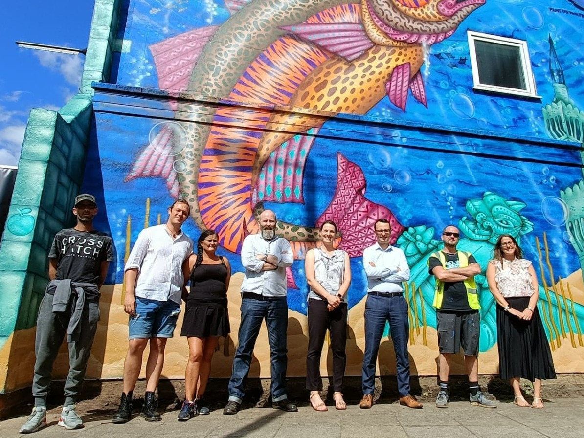 A group of people standing in front of a mural of a fish on a building.