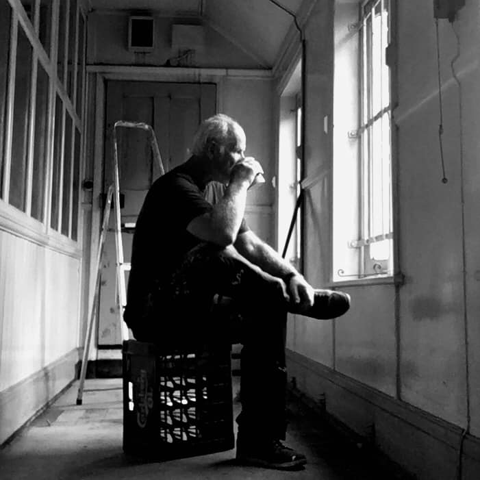 A man is sitting on a crate looking out a window