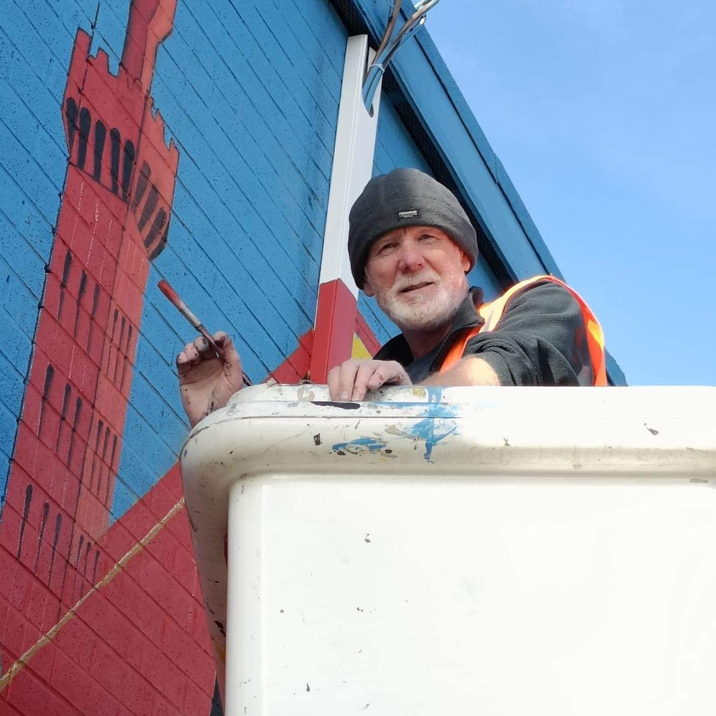 A man is painting a red white and blue mural on the side of a building