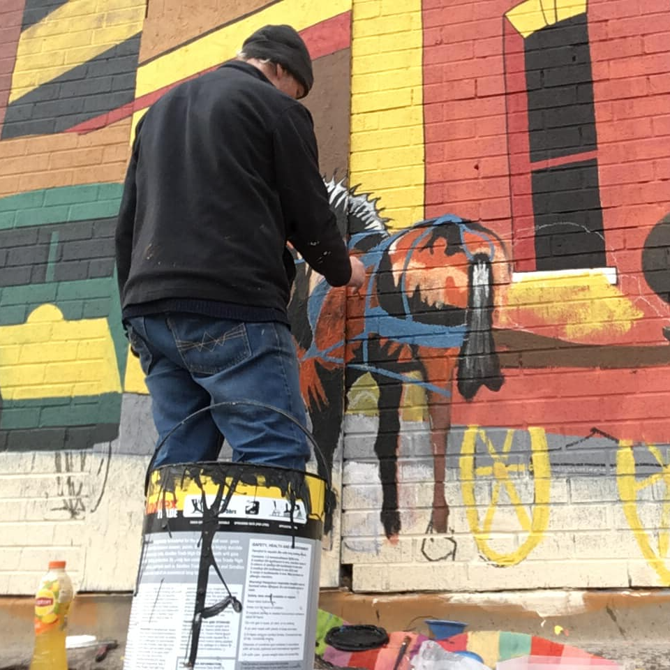 A man is painting a horse on a brick wall