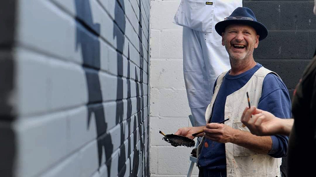 A man in a hat is laughing while standing next to a wall.