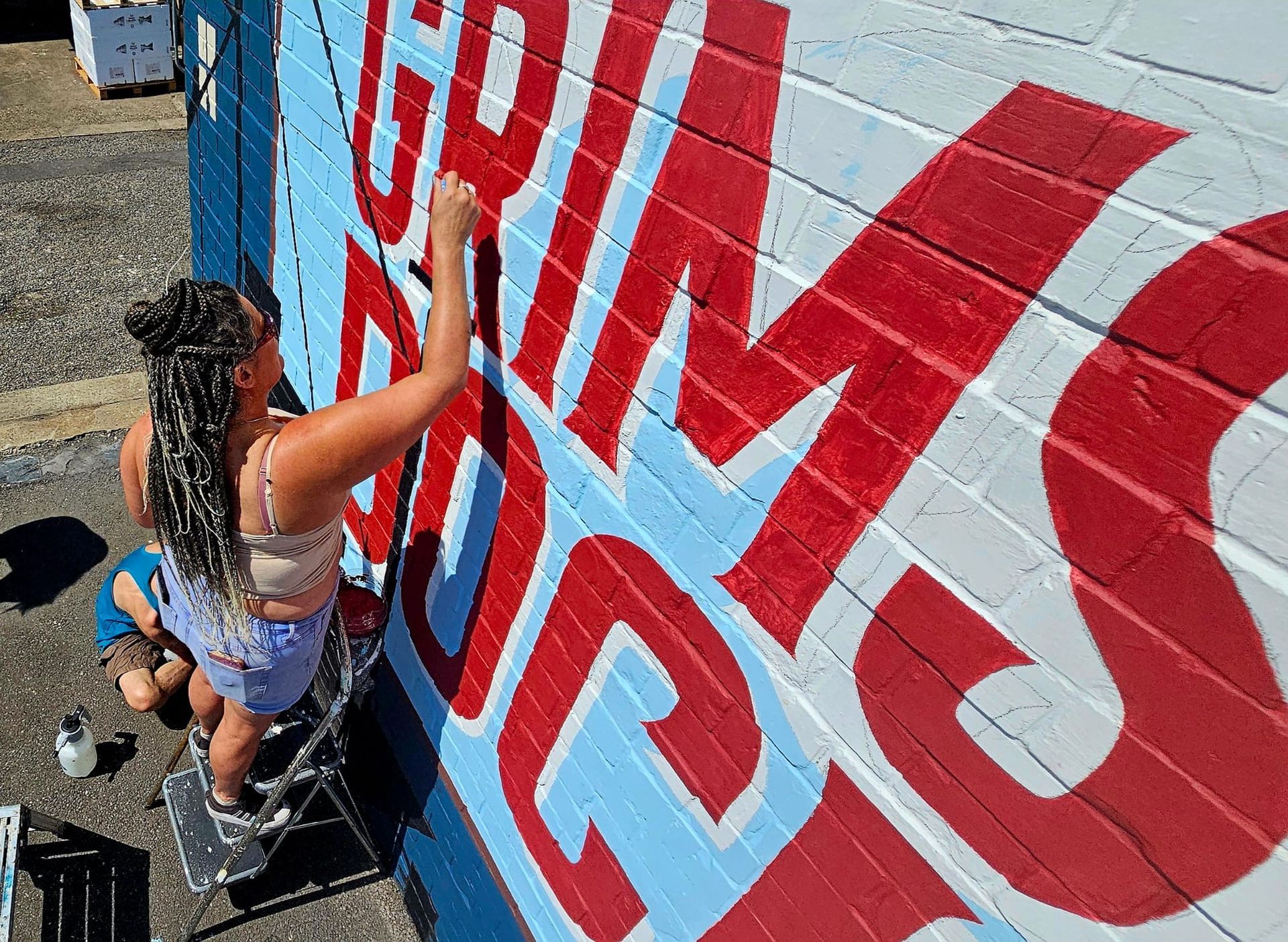 A woman is painting a mural on a brick wall.