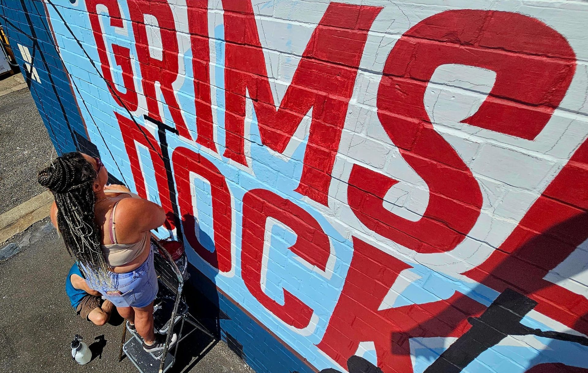 A woman is painting a mural on a brick wall.