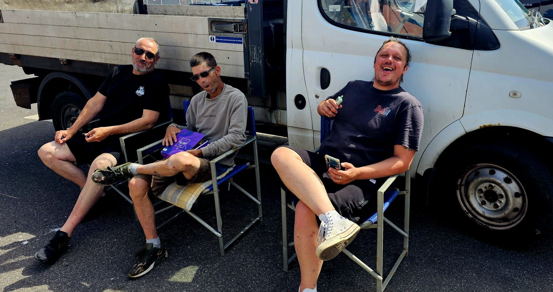 Three men are sitting in director 's chairs in front of a truck.