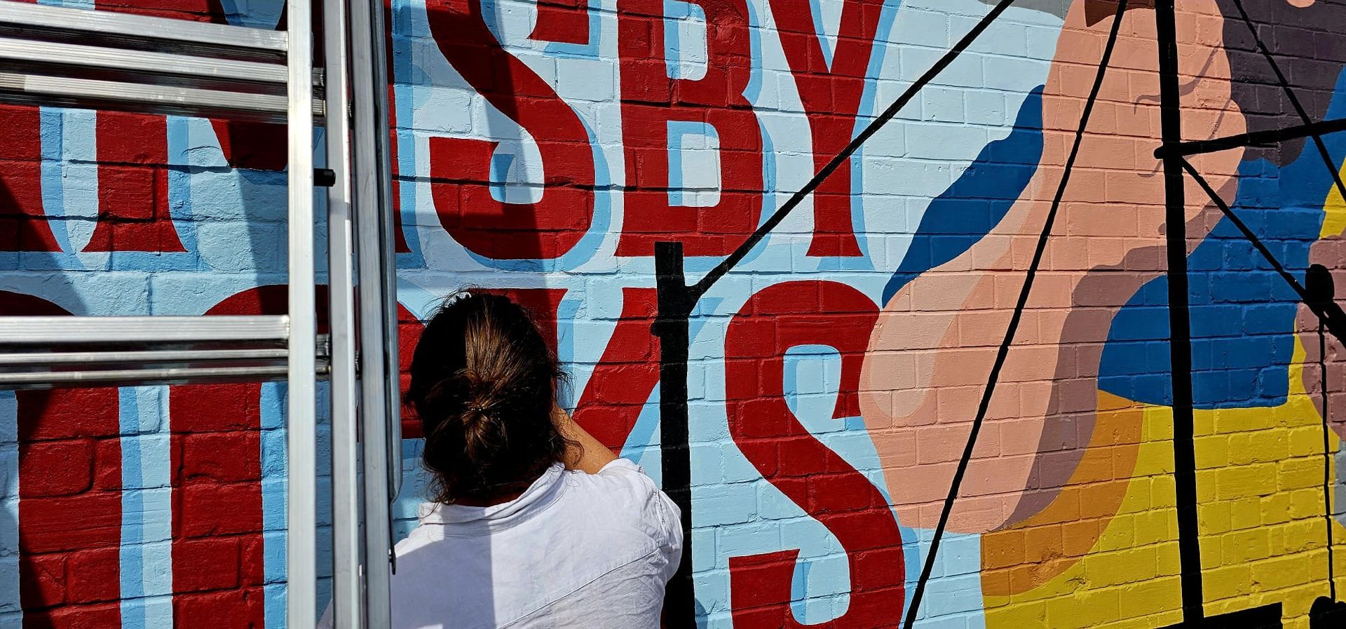 A woman is painting a mural on a brick wall.