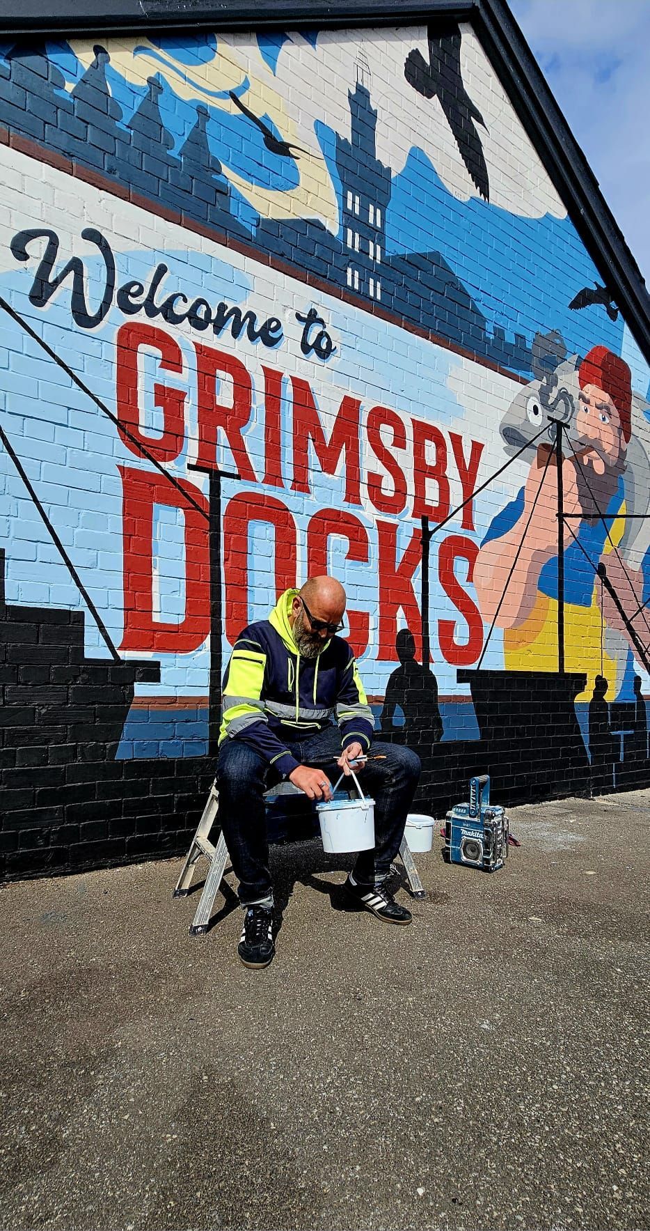 A man is sitting in front of a large mural on the side of a building.